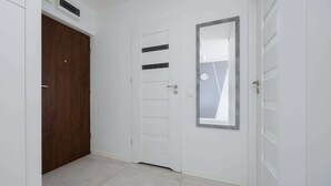 A hallway with a wooden door, a white door with horizontal slats, and a mirror on the wall.