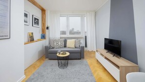 A modern living room with a grey sofa, a coffee table, a TV on a wooden stand, and a window with curtains.