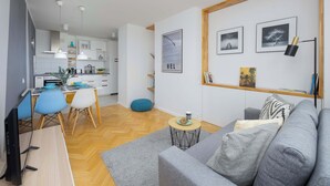 Una sala moderna con un sofá gris, una zona de comedor con sillas azules y una cocina al fondo.
