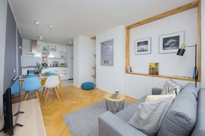 Una sala moderna con un sofá gris, una zona de comedor con sillas azules y una cocina al fondo.