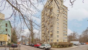 Un edificio residencial de varios pisos con balcones, coches aparcados y cielo despejado.