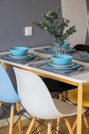 Una mesa de comedor dispuesta con cuencos y platos azules, rodeada de sillas con patas de madera y un florero con follaje verde.