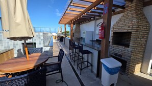 Une terrasse extérieure avec un four en briques, des tables et des chaises en bois.