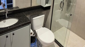 Une salle de bain moderne dotée d’une douche à parois de verre, de toilettes blanches, d’un lavabo sur plan noir et d’un meuble encastré.