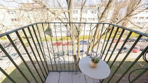 A balcony with a small table and a potted plant, overlooking a parking area and buildings.