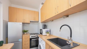 A compact kitchen with wooden cabinets, a built-in washing machine, a gas stove, a microwave, and a sink with a modern faucet.
