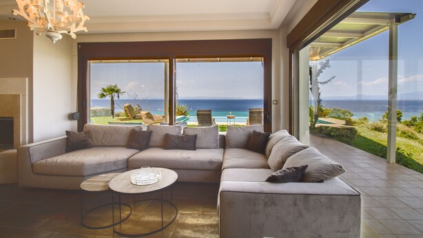 A modern living room with a large sectional sofa, a coffee table, and a view of the ocean through expansive windows.
