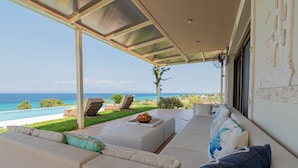 A modern outdoor seating area with a view of the sea, a pool, and a stone wall.