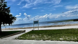 A beach with a sign, grassy area, and a pathway leading to the water.