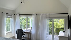 Une chambre spacieuse avec un grand lit, un bureau et un balcon offrant une vue sur la verdure.