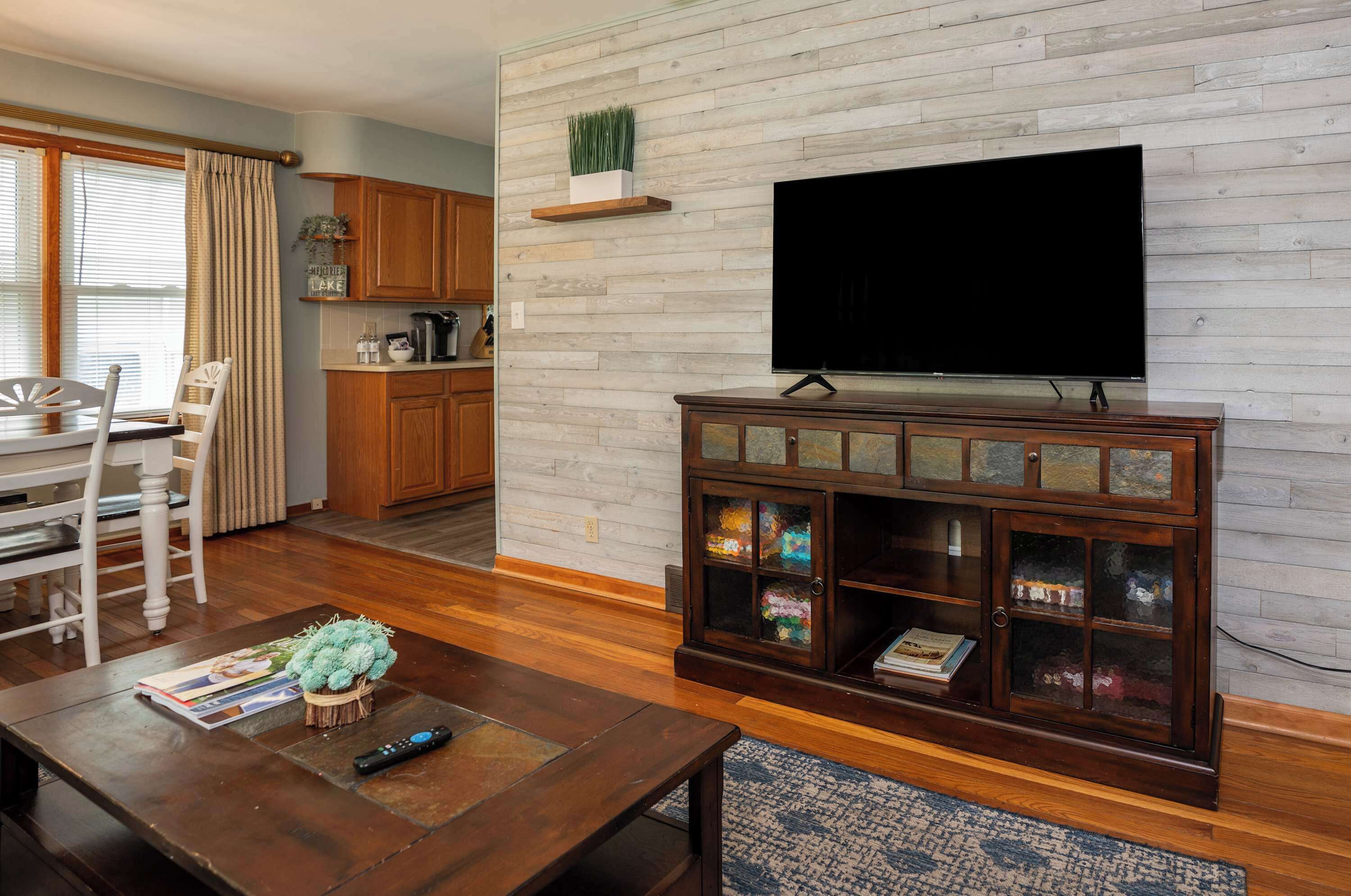 Ein Wohnzimmer mit einem HolztV-Schrank, einem Esstisch mit Stühlen und einer Küche mit Holzschränken.
