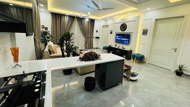 A modern living room with a central island, a flat-screen TV mounted on the wall, and a ceiling fan.