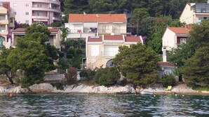 A coastal town with buildings along the waterfront, including a stone house with a red roof and a white building with balconies.