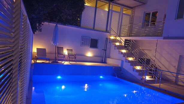 A swimming pool with a blue-lit water feature, a staircase with metal railings, and a seating area with two chairs and a table.