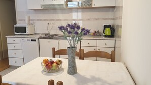 A kitchen with white cabinets, a microwave, a coffee maker, and a vase with flowers on the table.