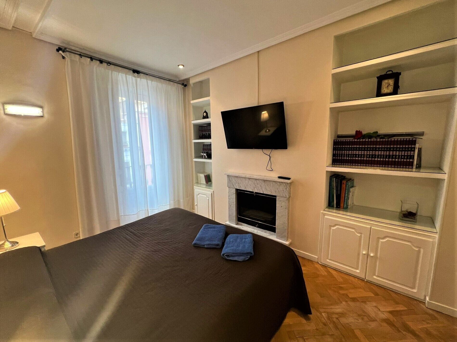 A hotel room with a bed, a TV mounted above a fireplace, and built-in bookshelves.