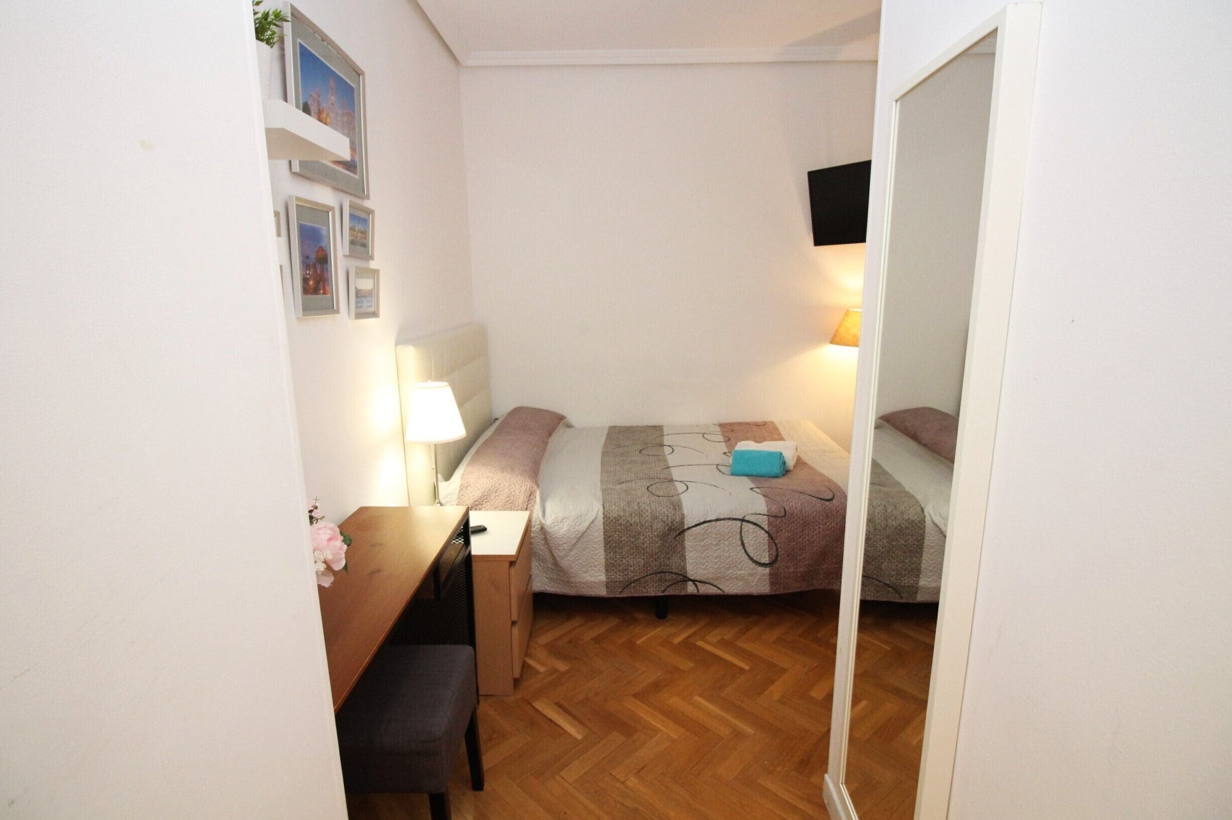 A small, neatly arranged bedroom with a bed, a desk, and a chair.