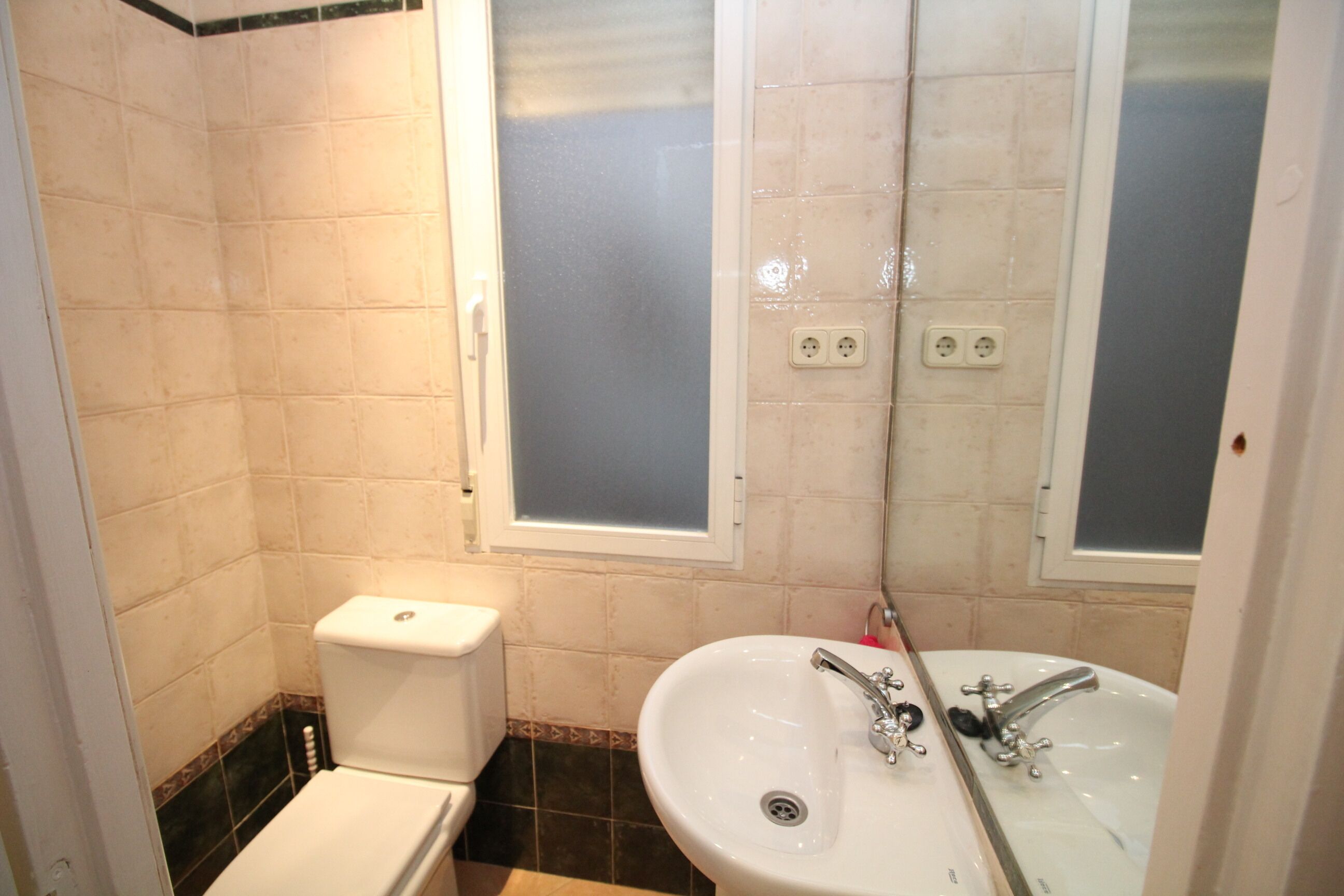 Un baño con inodoro, lavamanos y dos ventanas.