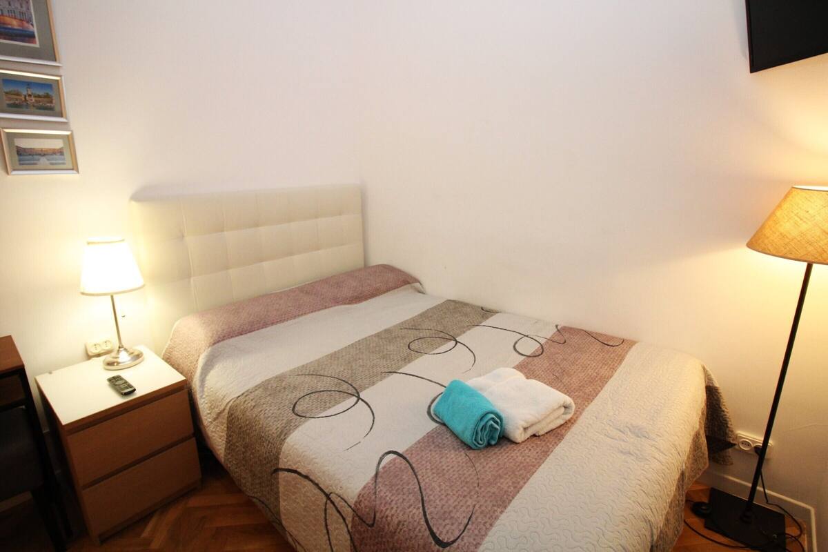 Un lit bien fait, avec une couvre-lit à rayures, une lampe de chevet et une serviette pliée posée sur le lit.