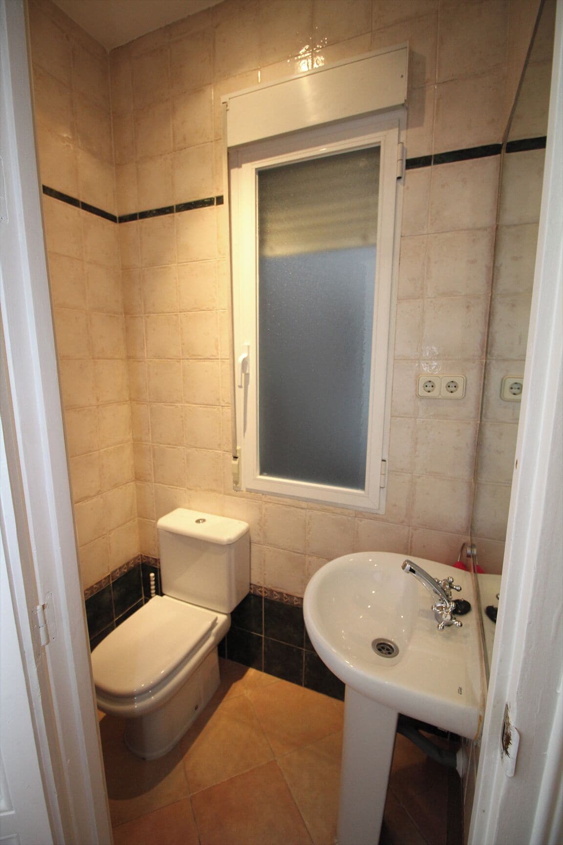 A small bathroom with a toilet, sink, and a window above the sink.