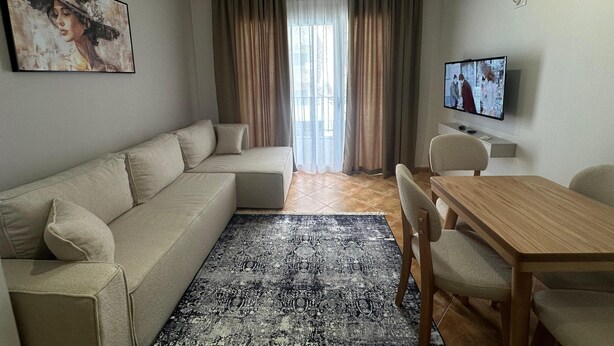 A modern living room with a sofa, a patterned rug, a wooden dining table, and a TV. - Palm Suites Apartaments (Vlore)