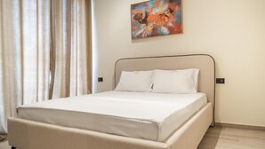 A neatly made bed with a headboard, a painting on the wall, and a window with curtains. - Palm Suites Apartaments (Vlore)
