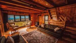 Un intérieur de chalet chaleureux avec une grande fenêtre offrant une vue panoramique, une cheminée et un coin salon confortable.