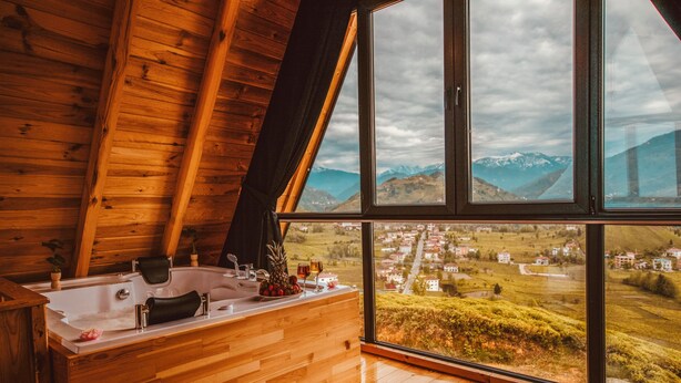 Une cabane en bois dotée d’une grande fenêtre donnant sur une ville et des montagnes.