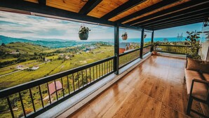 Un balcon en bois offrant une vue sur un paysage verdoyant et sur des lignes électriques éloignées.
