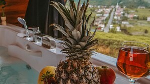 Une table avec un ananas, des fraises et un verre d’une boisson rouge, avec vue sur une ville à travers une fenêtre.