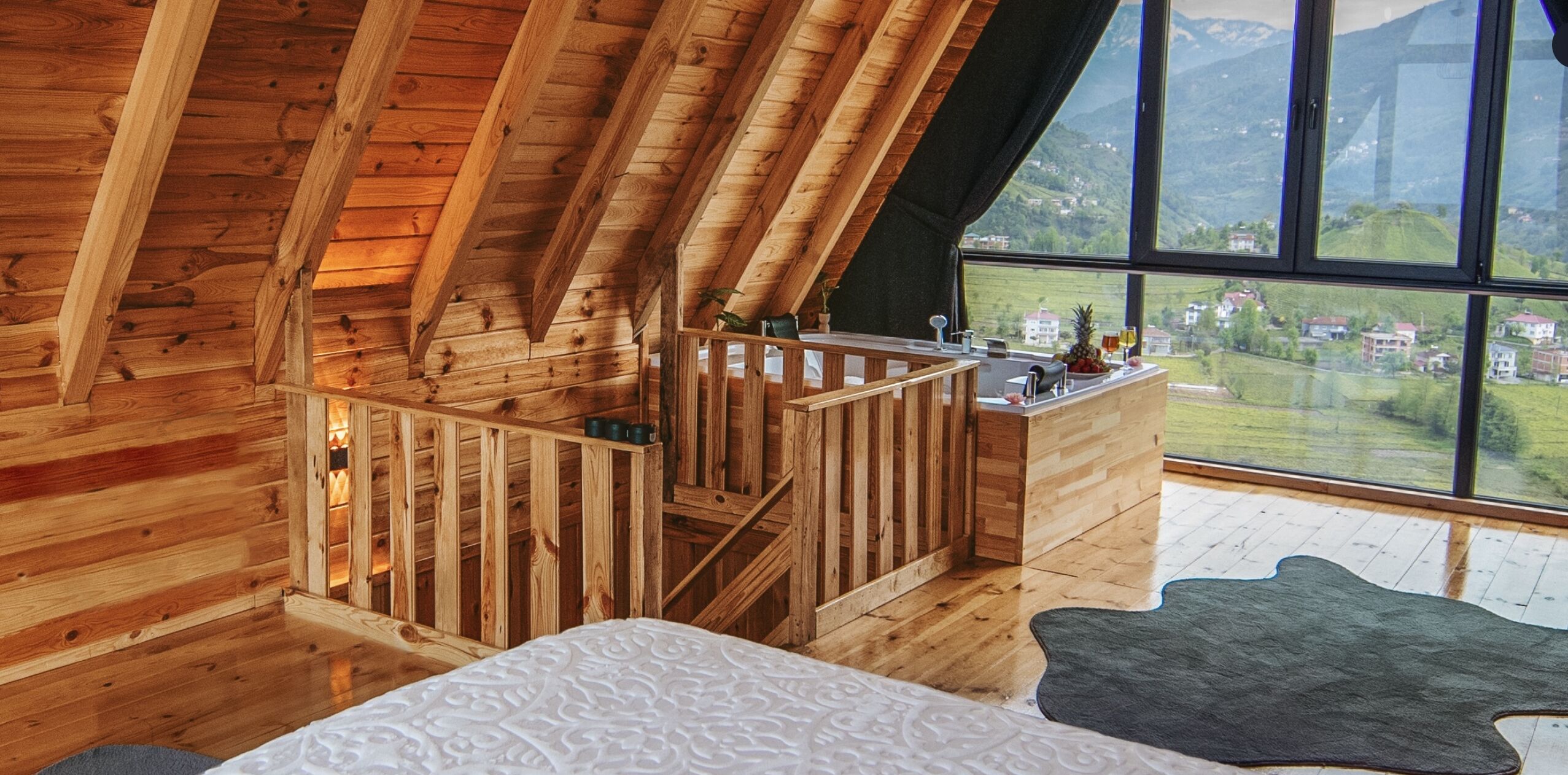 Una cabaña de madera con habitación en el altillo, una kitchenette pequeña y un ventanal con vistas al campo.