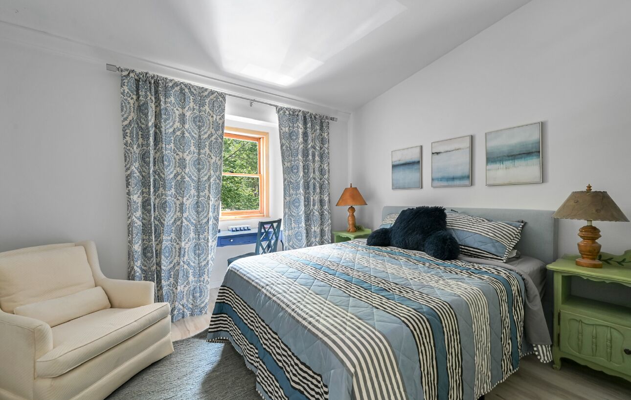 Un dormitorio con cama, una silla, una mesita de noche y una ventana con cortinas.
