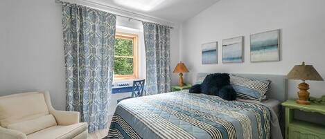 Un dormitorio con cama, una silla, una mesita de noche y una ventana con cortinas.