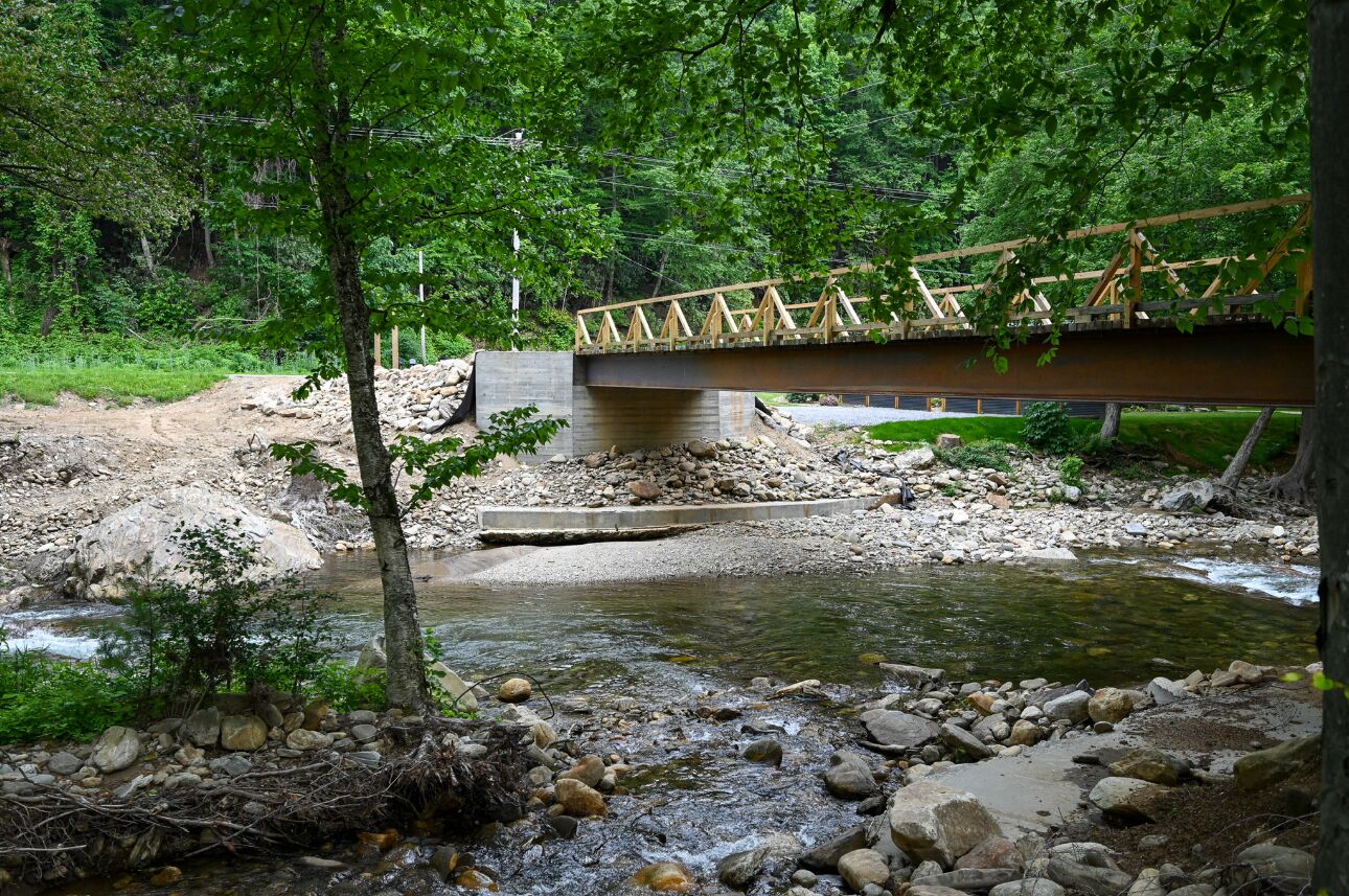 A wooden bridge over a rocky stream in a forested area.
