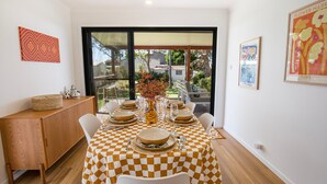 Un coin repas avec une nappe à carreaux, un buffet en bois et une vue sur un jardin extérieur, visible à travers une porte vitrée.