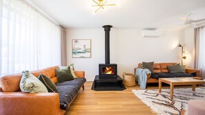 Un salon chaleureux avec un poêle à bois central, des canapés en cuir, une table basse en bois et un tapis à motifs.