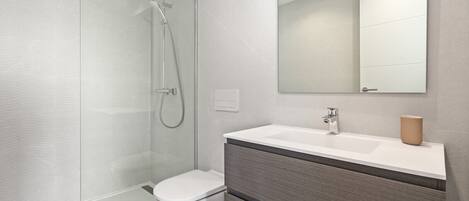 Un bagno moderno con doccia vetrata, vaso bianco e mobile lavabo con specchio e contenitore color beige.