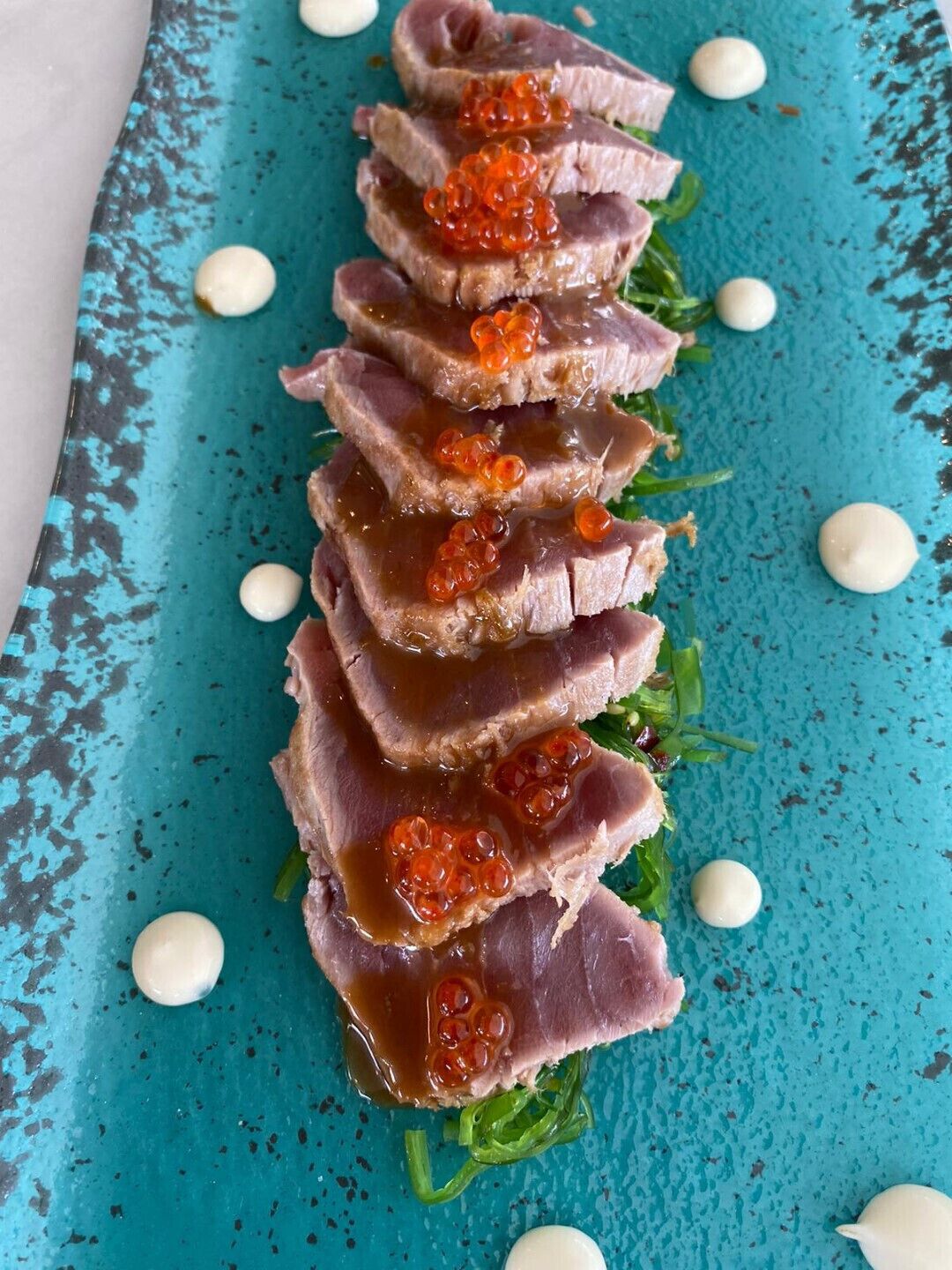Un plato de carne en rodajas con caviar y puntos de crema sobre un plato azul.