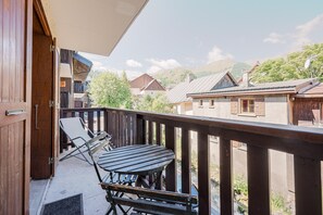 A balcony with a table and chairs, a wooden door, and a view of surrounding buildings and hills.