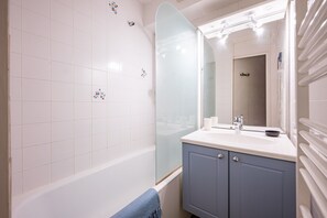 A bathroom with white tiles, a glass shower enclosure, a sink with a mirror, and a towel rack.