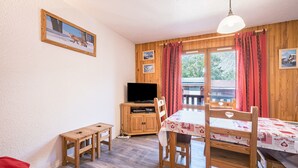 A room with a wooden table, chairs, a television on a wooden cabinet, and a window with curtains.