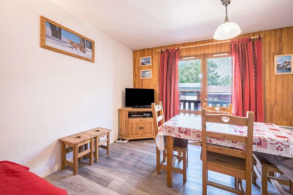 A room with a wooden table, chairs, a television on a wooden cabinet, and a window with curtains.