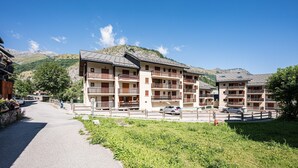 A multi-story hotel with balconies, a paved driveway, and a mountainous backdrop.