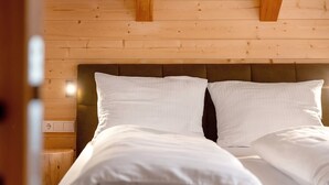 A bed with white linens and a wooden headboard in a room with wooden walls.