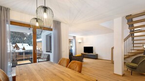 A modern living room with a wooden dining table, comfortable seating, a TV, and a staircase.