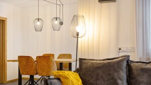 A modern living room with a sofa, a dining table with chairs, and pendant lighting.