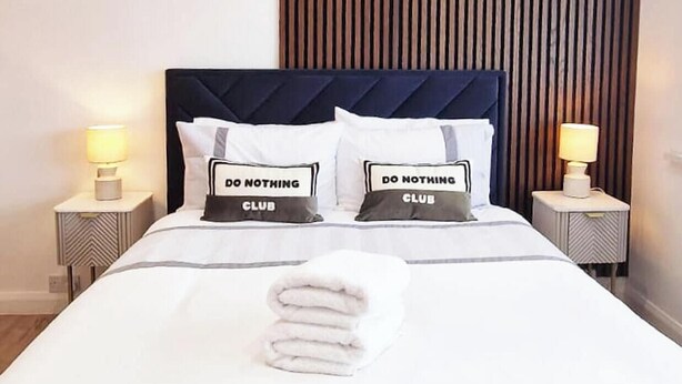 Een hotelkamer met een bed, twee nachtkastjes, een aan de muur hangend kunstwerk en een houten paneel.