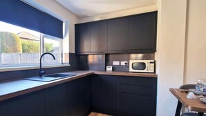 Een moderne keuken met donkere kastjes, een ingebouwde magnetron en een raam met een zwart rolgordijn.