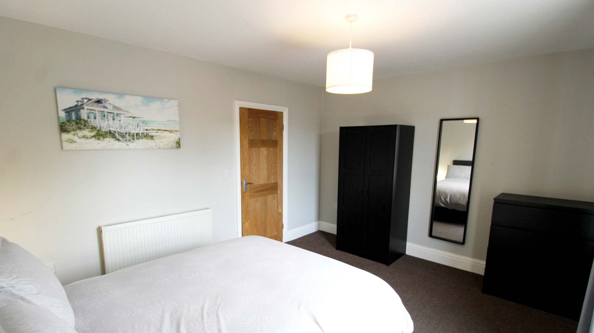 Une chambre à coucher avec un lit, une porte en bois, une armoire noire, un miroir et un tableau accroché au mur.