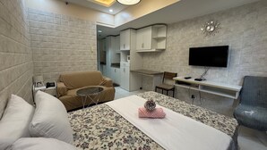 A hotel room with a bed, a sofa, a small table, a TV, and a kitchenette.